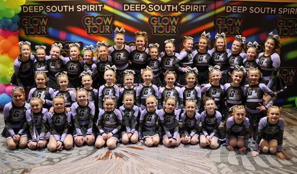 A group of cheerleaders are posing for a picture in front of a sign that says deep south spirit