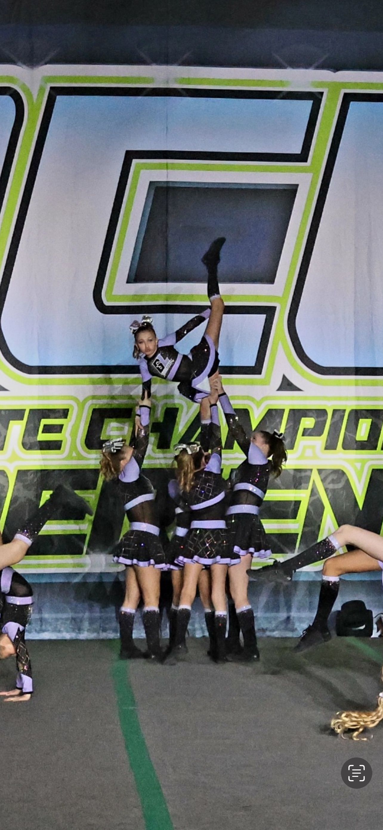 A group of cheerleaders are doing a handstand in front of a large sign.