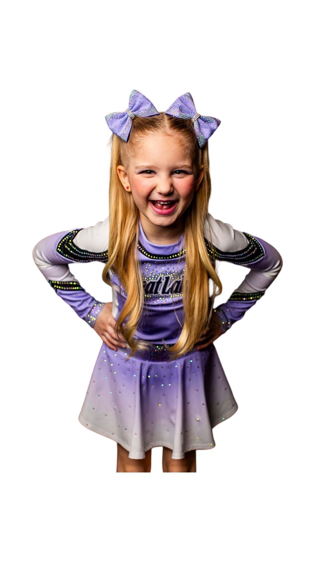 A little girl in a cheerleading uniform is standing with her hands on her hips.
