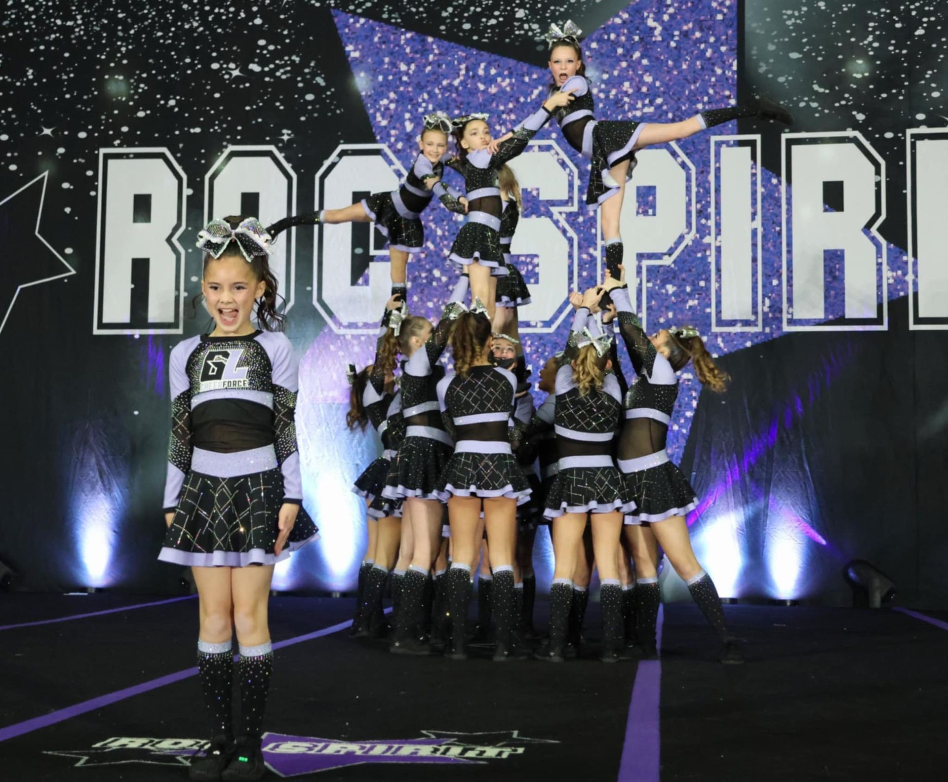 A group of cheerleaders are performing in front of a sign that says rock spirit