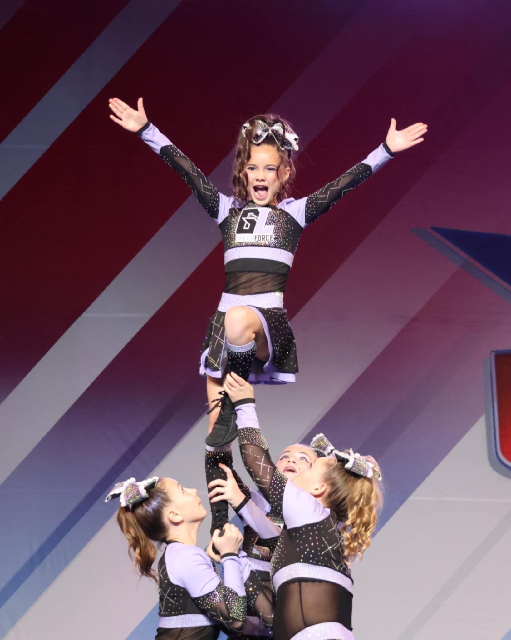 A cheerleader is being lifted in the air by two other cheerleaders