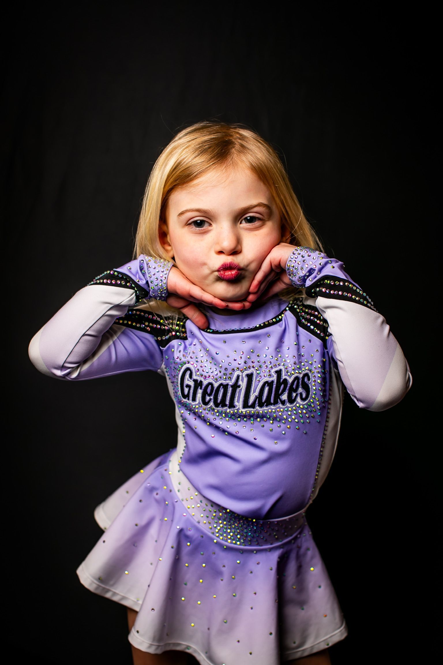 A little girl in a purple cheerleading uniform is making a funny face.