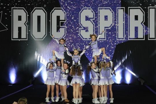 A group of cheerleaders are performing in front of a sign that says roc spirit