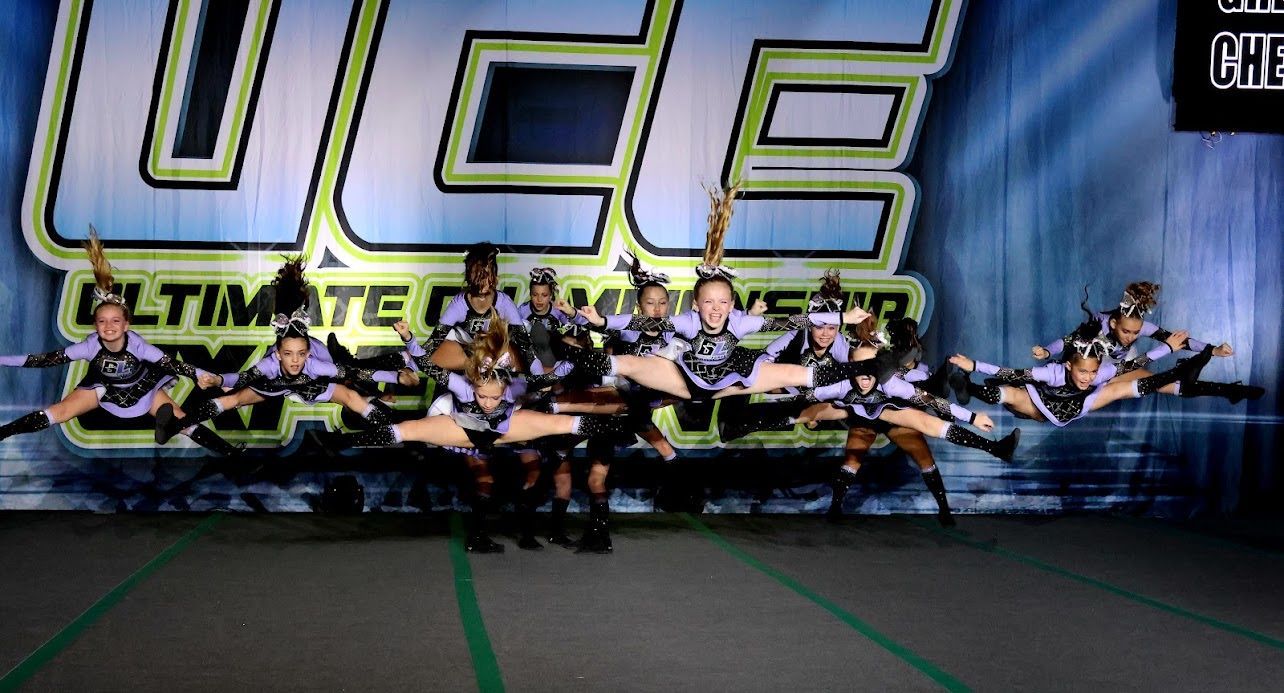 A group of cheerleaders are performing on a stage in front of a banner that says ultimate cheer.