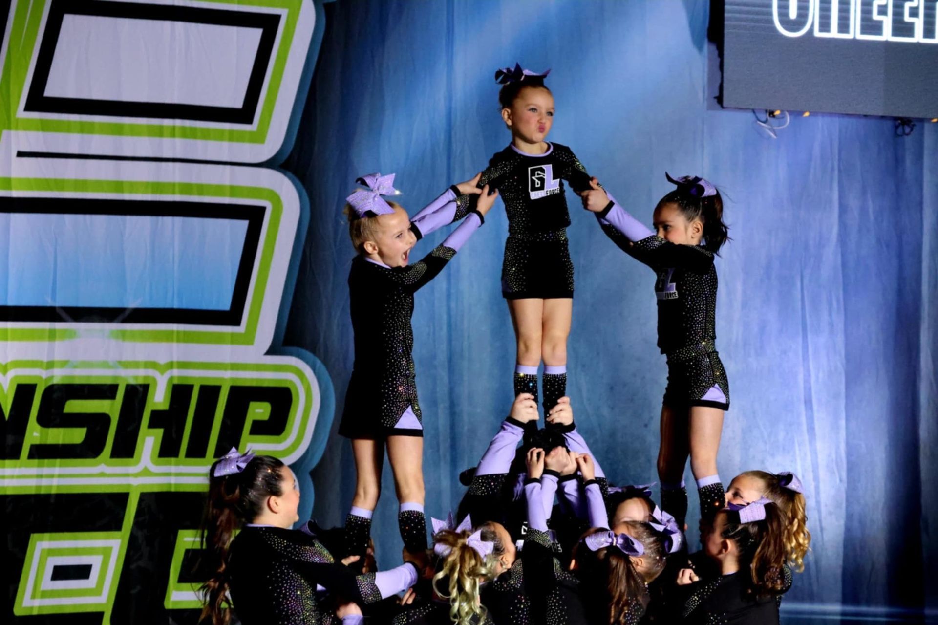 A group of cheerleaders are doing a pyramid on a stage in front of a sign