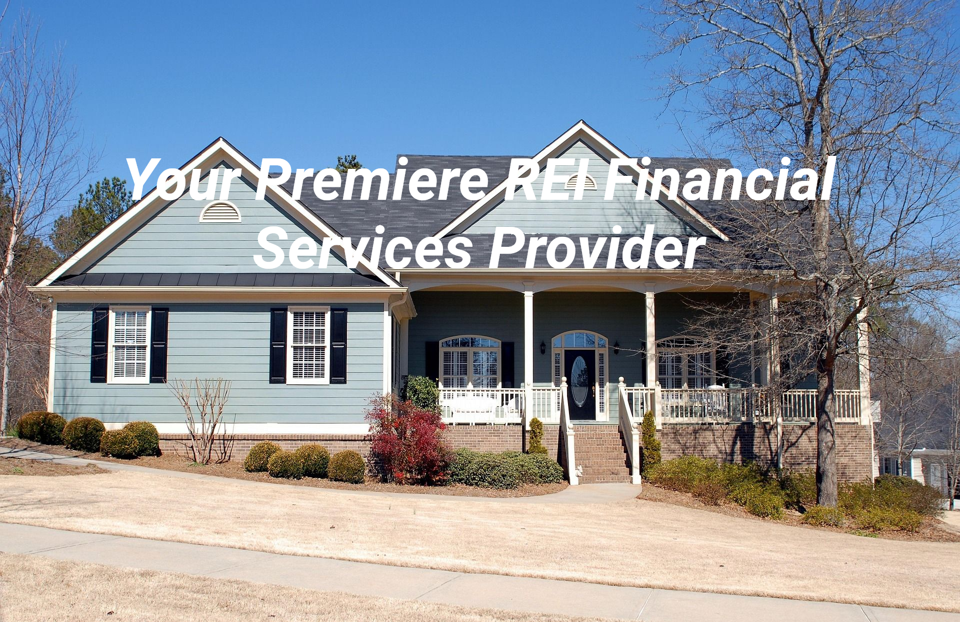 Blue house with dark roof and porch; landscaping with small bushes and a tree.