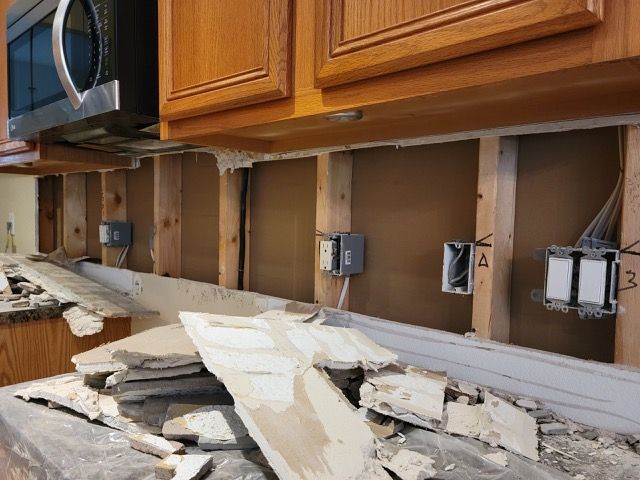 A kitchen is being remodeled with wooden cabinets and a microwave.