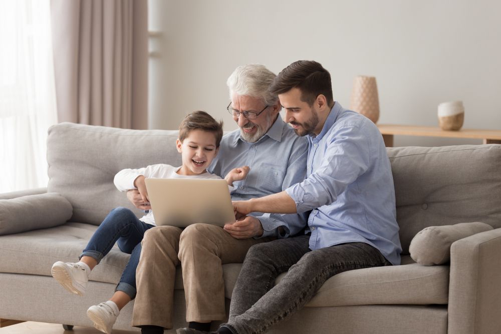 Three Generations Viewing Laptop: Boy, Grandfather, And Father On A Sofa — Shane Kelly Communications in Northern Rivers, NSW