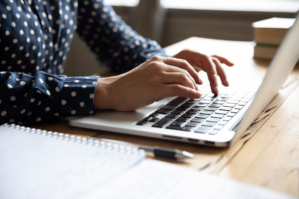 Person Typing On A Laptop At A Desk; A Notebook And Pen Are Nearby — Shane Kelly Communications in Northern Rivers, NSW