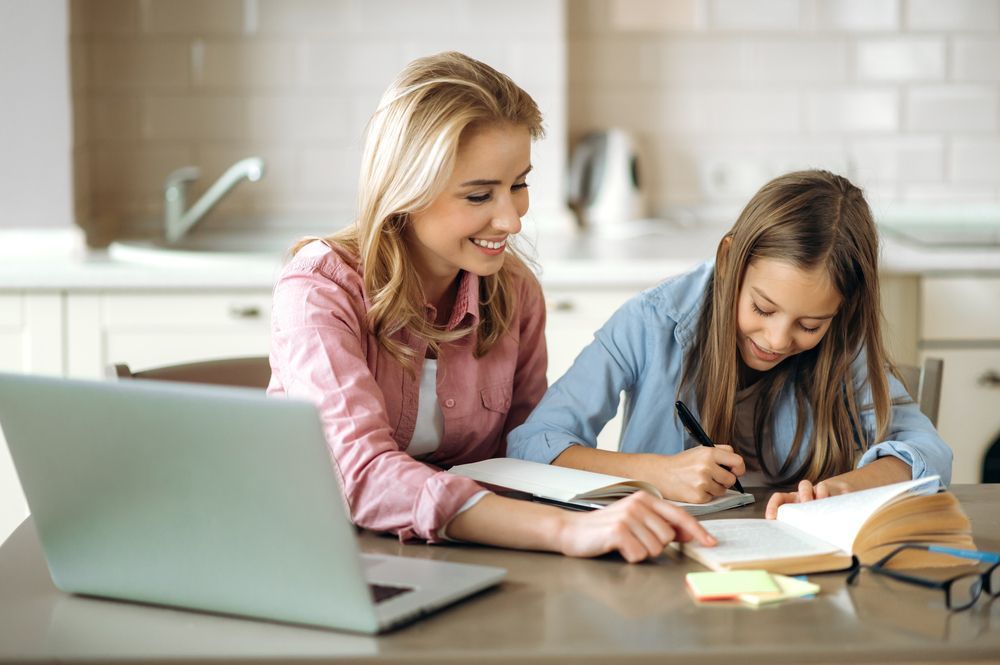 Woman Helps Girl With Homework At A Kitchen Table; A Laptop Sits Nearby — Shane Kelly Communications in Northern Rivers, NSW