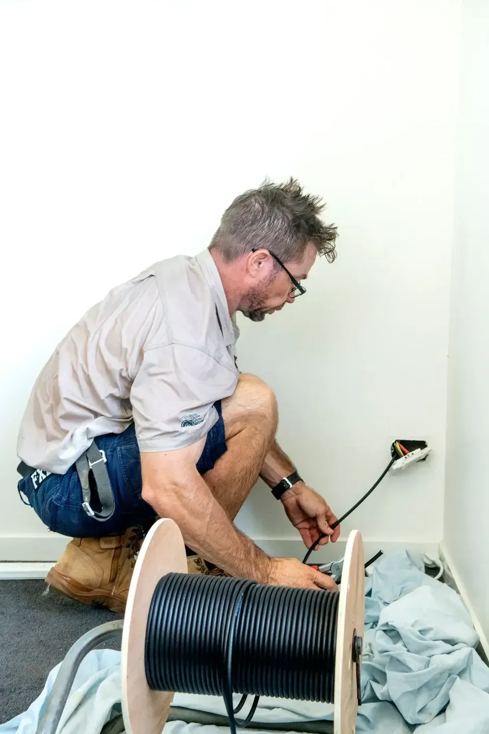 A Man Installing A Cable, Squatting Near An Electrical Outlet — Shane Kelly Communications in Northern Rivers, NSW