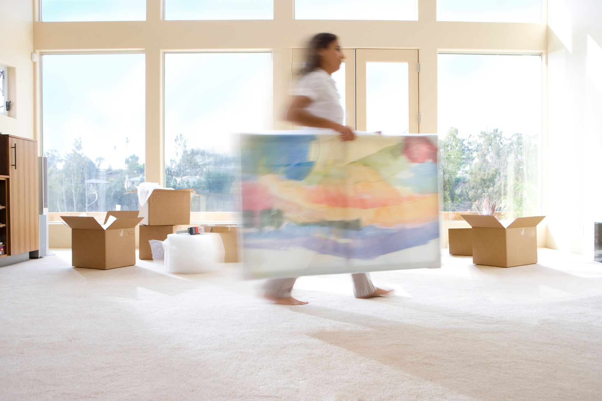 A woman is carrying a large painting in a living room