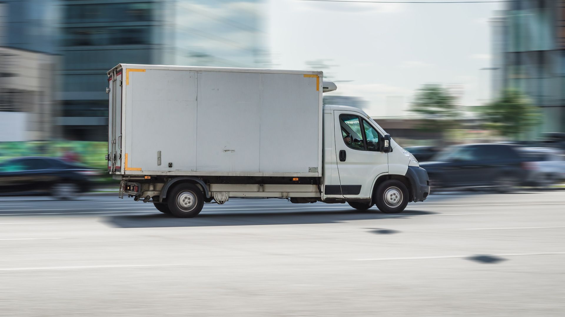 A white delivery truck is driving down a city street.