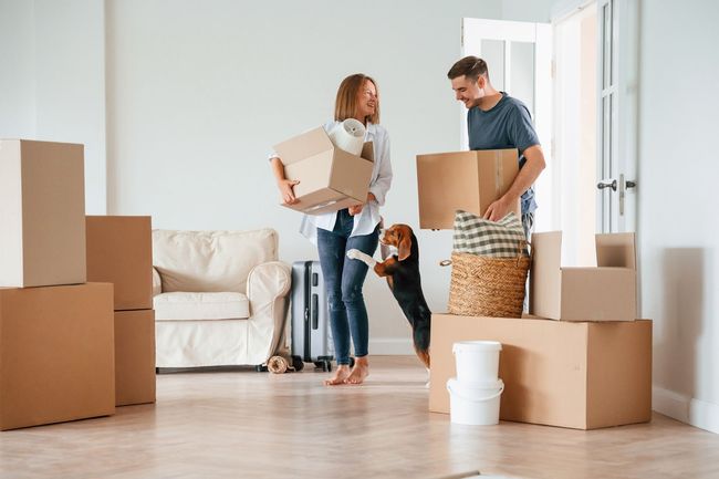 A family is moving into a new home while holding boxes and a dog.