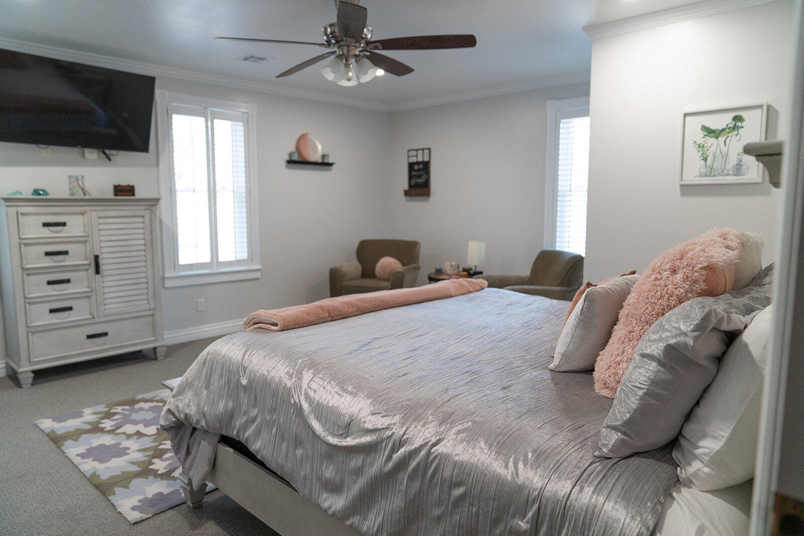 Bedroom with bed, dresser, armchairs, and window. Gray and white decor with pink accents.