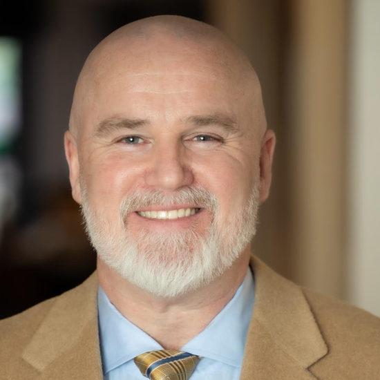 A bald man in a suit and plaid shirt is smiling for the camera.