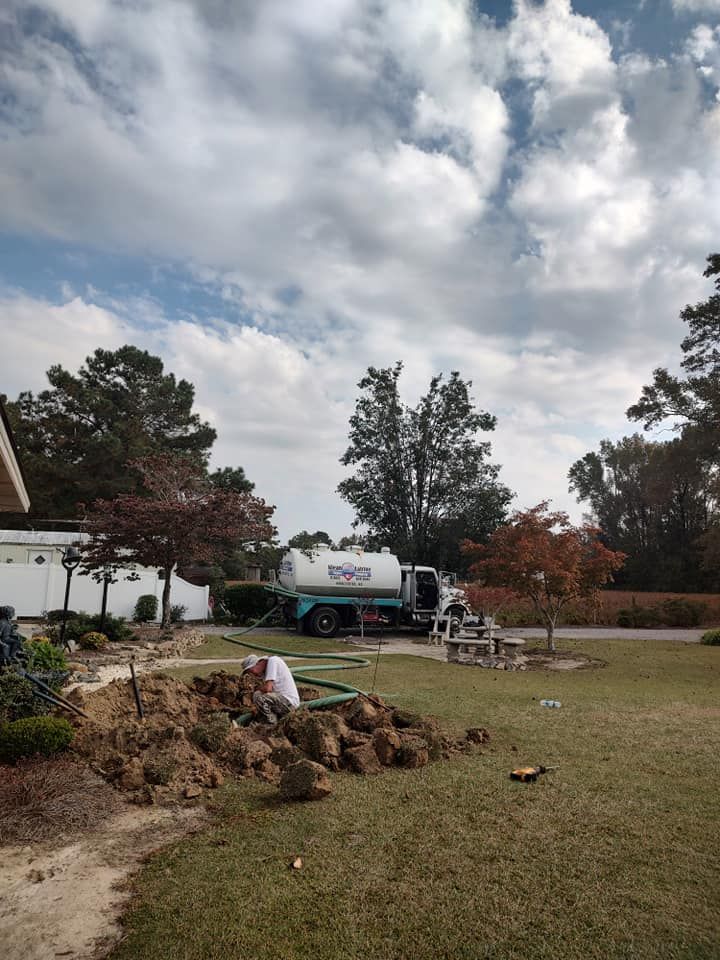 A septic tank truck is parked in the grass in front of a house.
