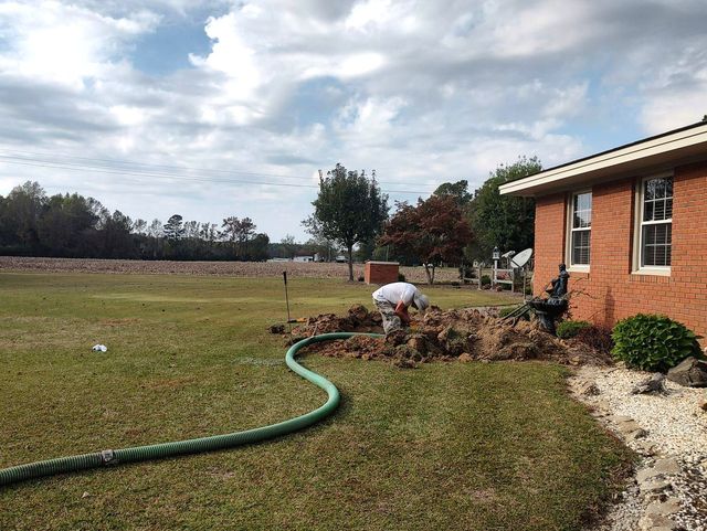 A man is digging in the dirt in front of a brick house.