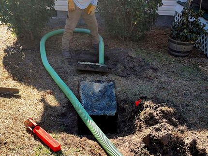 A man is pumping water into a septic tank with a green hose.