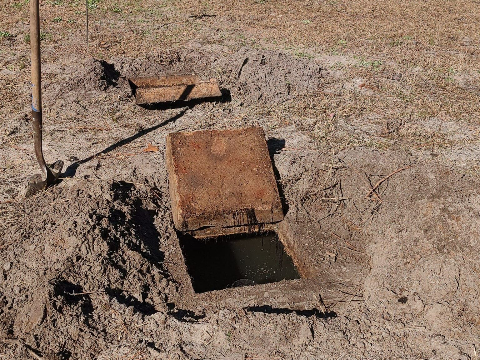 A wooden box is sitting in the dirt next to a shovel.