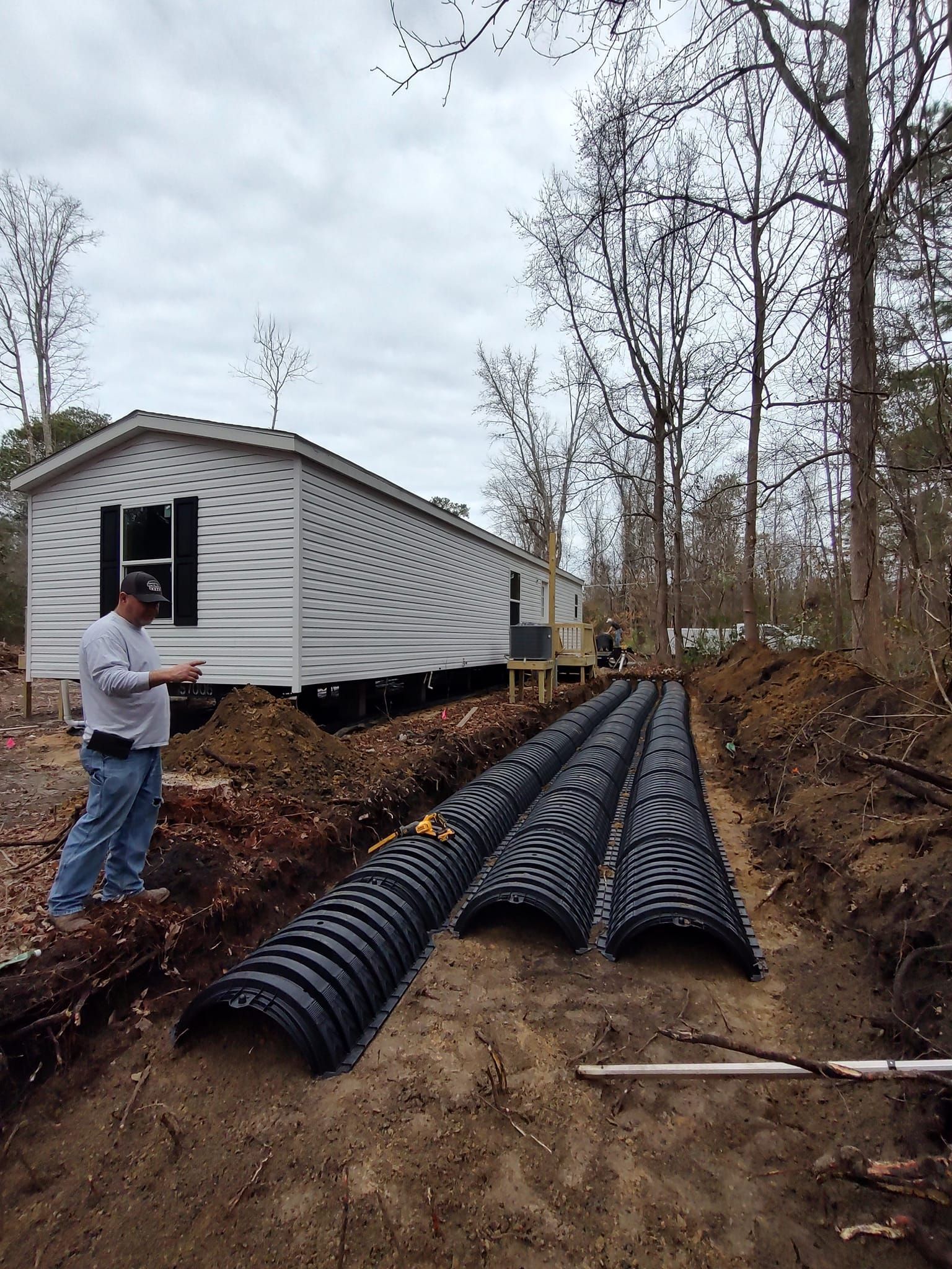 A man is standing in the dirt in front of a mobile home.