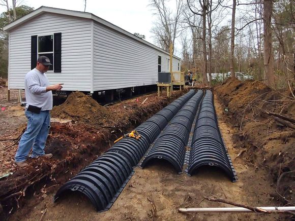 A man is standing in a trench next to a mobile home