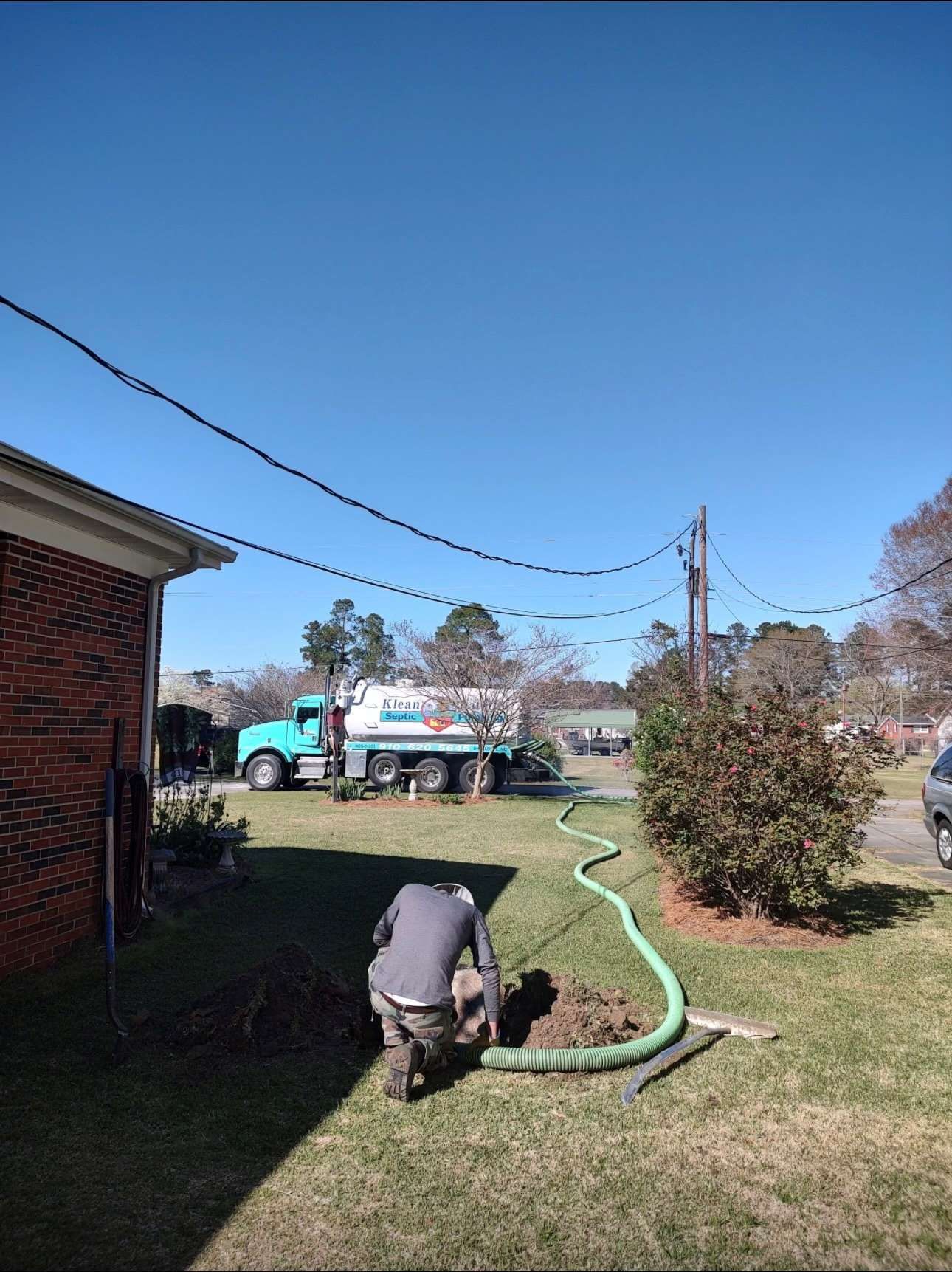 A man is kneeling in front of a septic tank with a truck in the background.