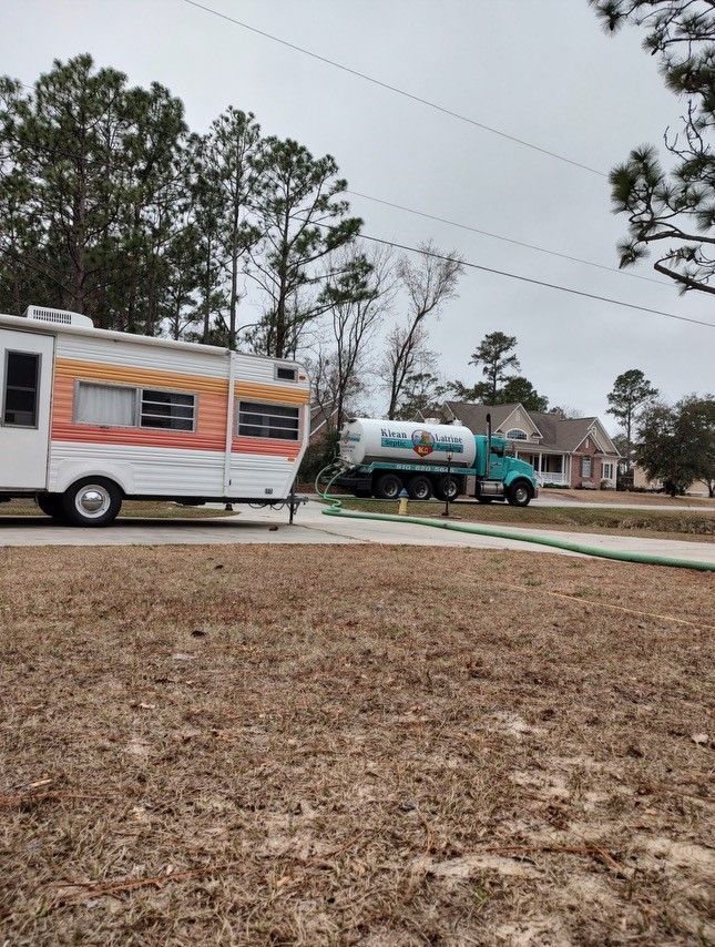 A rv is parked next to a tanker truck in a field.