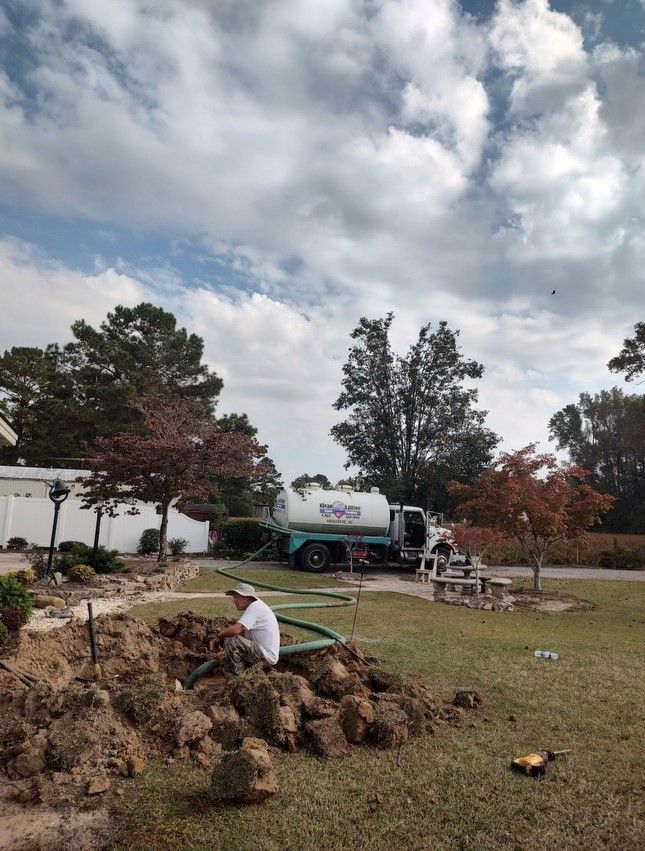 A man is sitting on a pile of dirt in front of a septic tank truck.