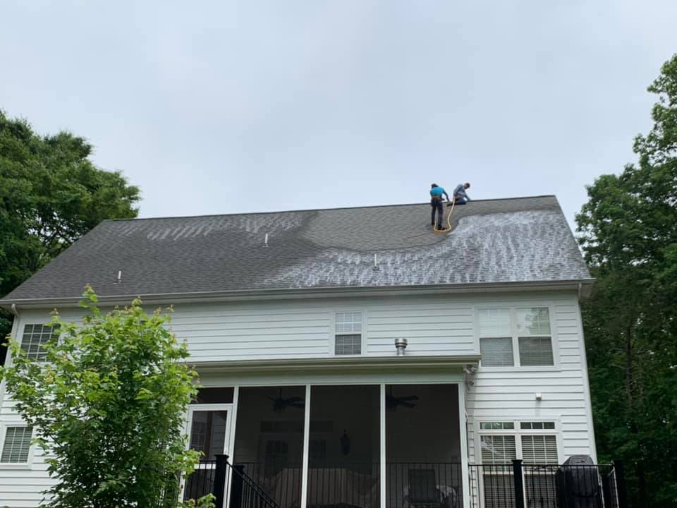 Two men are doing a shingle coating the roof of a house.