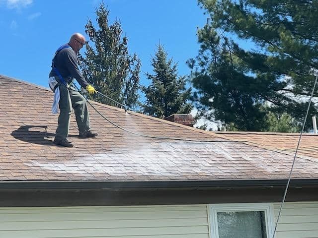 A man is spraying Fresh Roof on the roof of a house.