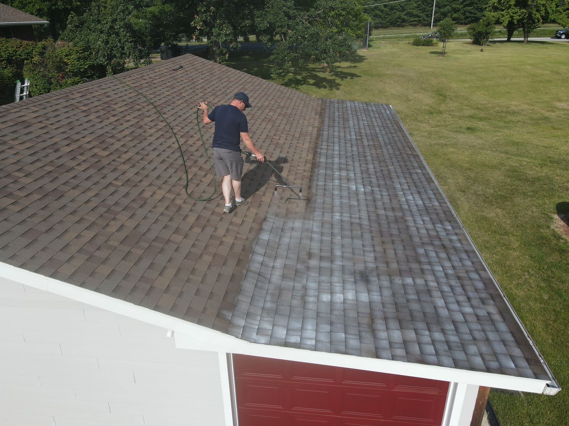 A man spraying roof rejuvenation spray on the roof of a house.