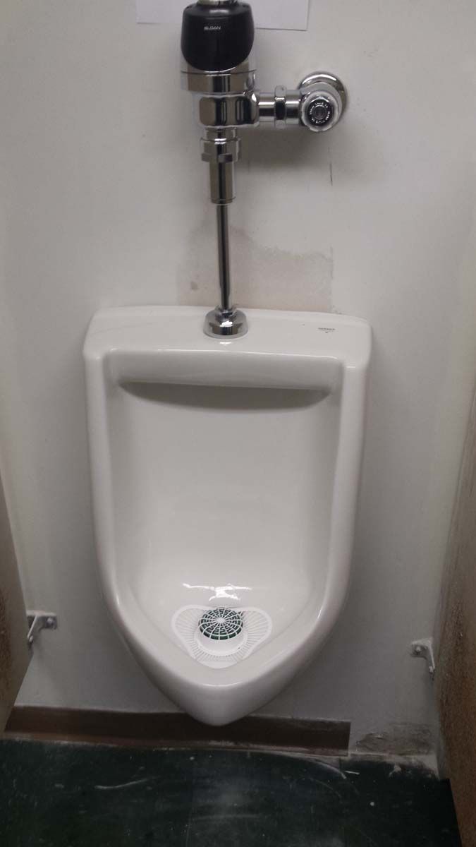 White urinal in a public restroom, with chrome flush valve and black sensor.