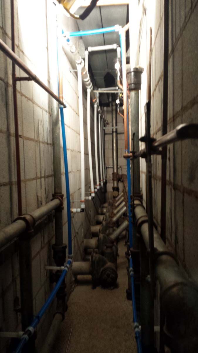 Narrow utility corridor with pipes and equipment, industrial setting.