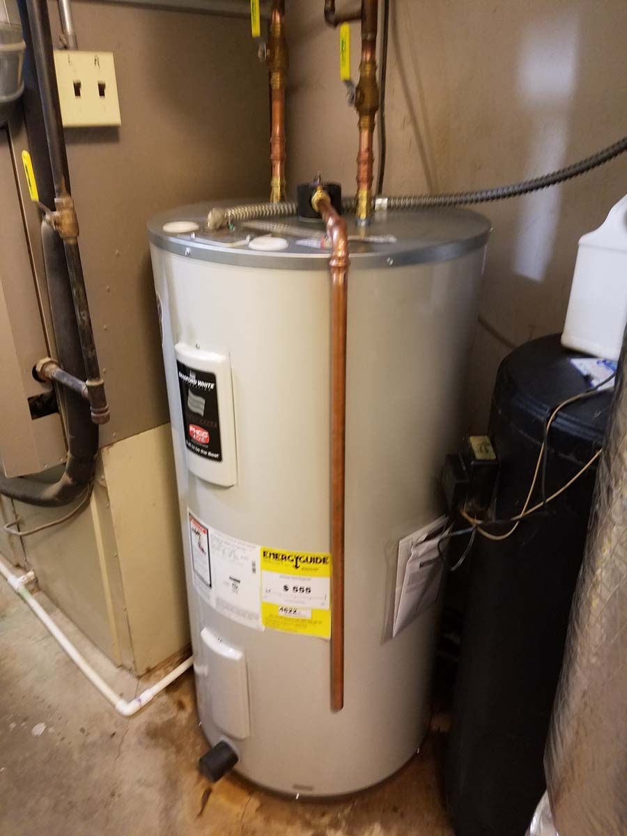 A cylindrical water heater with copper pipes in a utility room with a softener.
