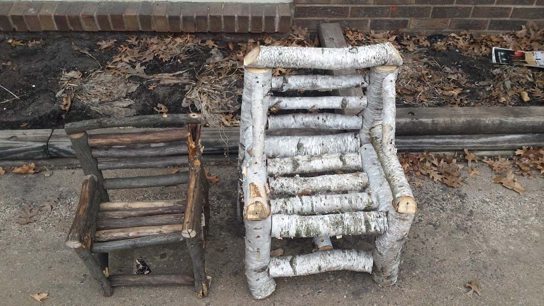 Two rustic wooden chairs sit side-by-side on a concrete surface, likely outdoors.