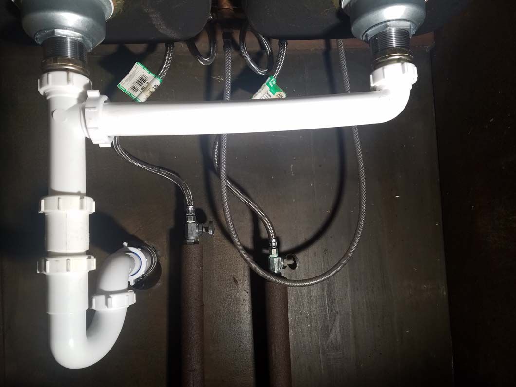 White sink plumbing beneath a sink, including a P-trap, pipes, and drain connections.