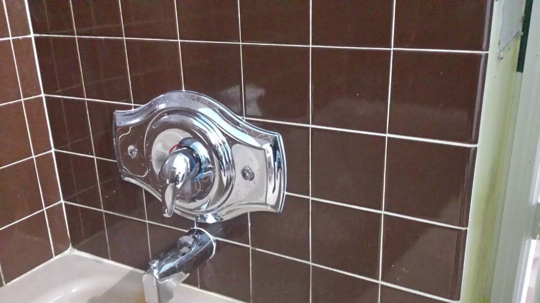 Silver shower faucet on brown tiled wall.