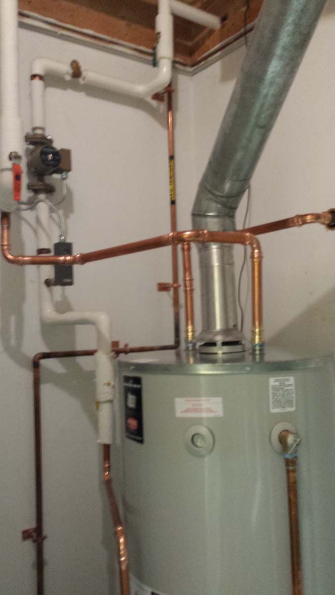 A water heater with copper piping, ventilation, and control panel installed in a corner of a room.