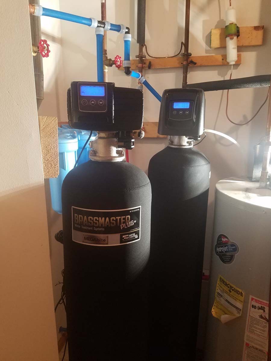 Water softener system in a utility room. Black tanks with digital control panels and blue piping.