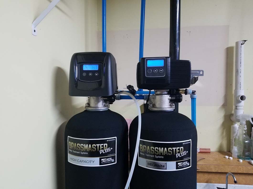 Two black water filtration systems with blue pipes against a light-colored wall.