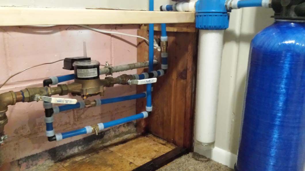 Plumbing system with water meter, filtration, and blue pipes in a basement.