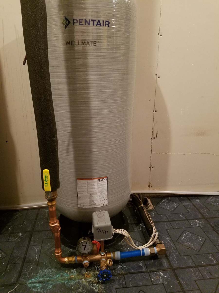 Water pressure tank with copper piping and insulation against a wall.