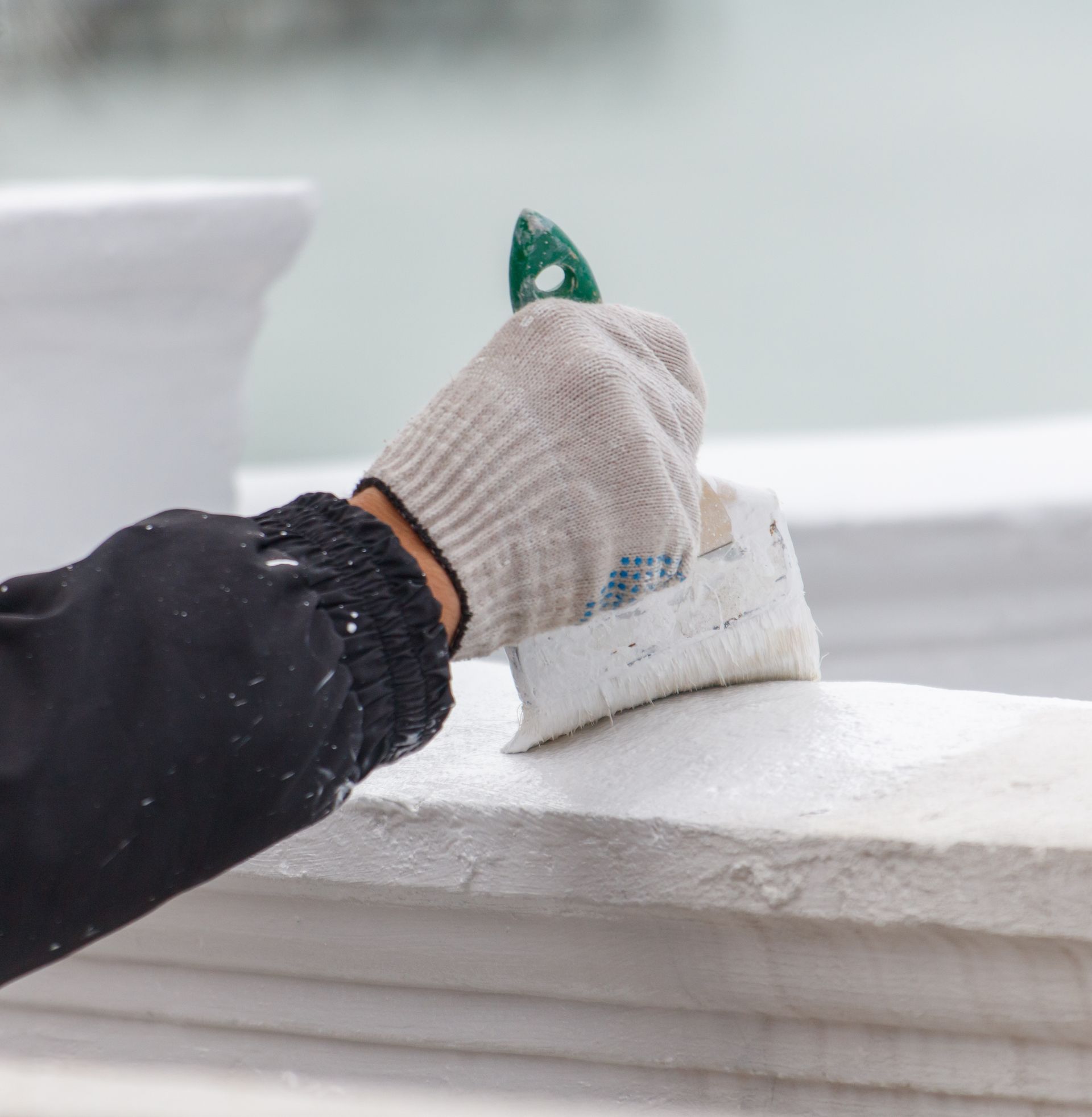 Person in work gloves painting a white surface with a brush.