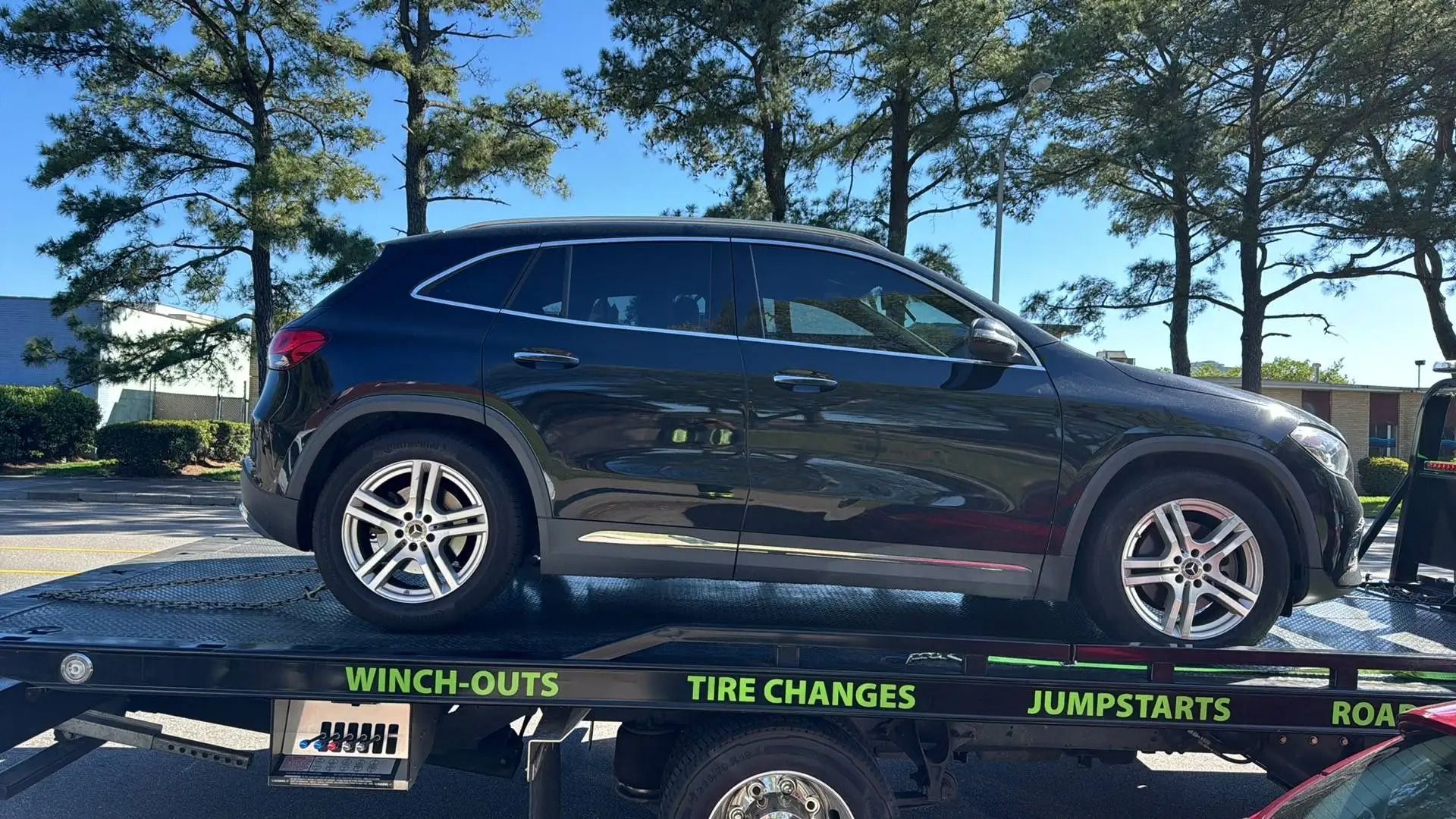 Black Mercedes SUV on a tow truck, parked outdoors on a sunny day.