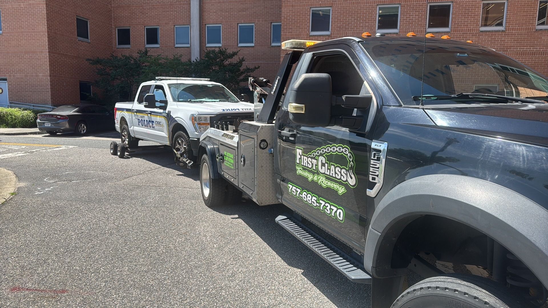 Tow truck towing a white pickup truck near a brick building.