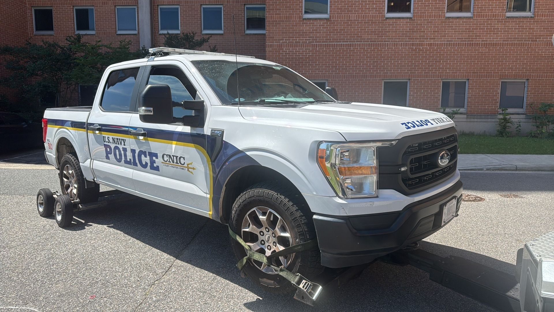 White police pickup truck on a tow truck in front of a brick building.
