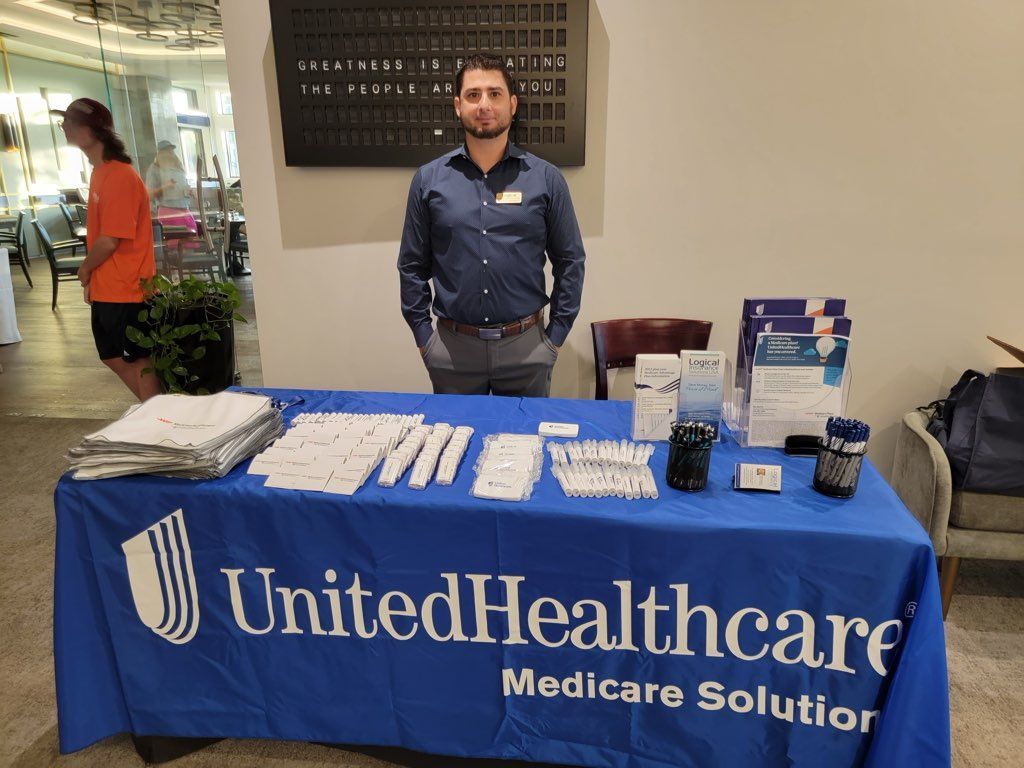 Man at a UnitedHealthcare Medicare Solutions table. He is wearing a blue shirt, and the table is blue with white lettering.