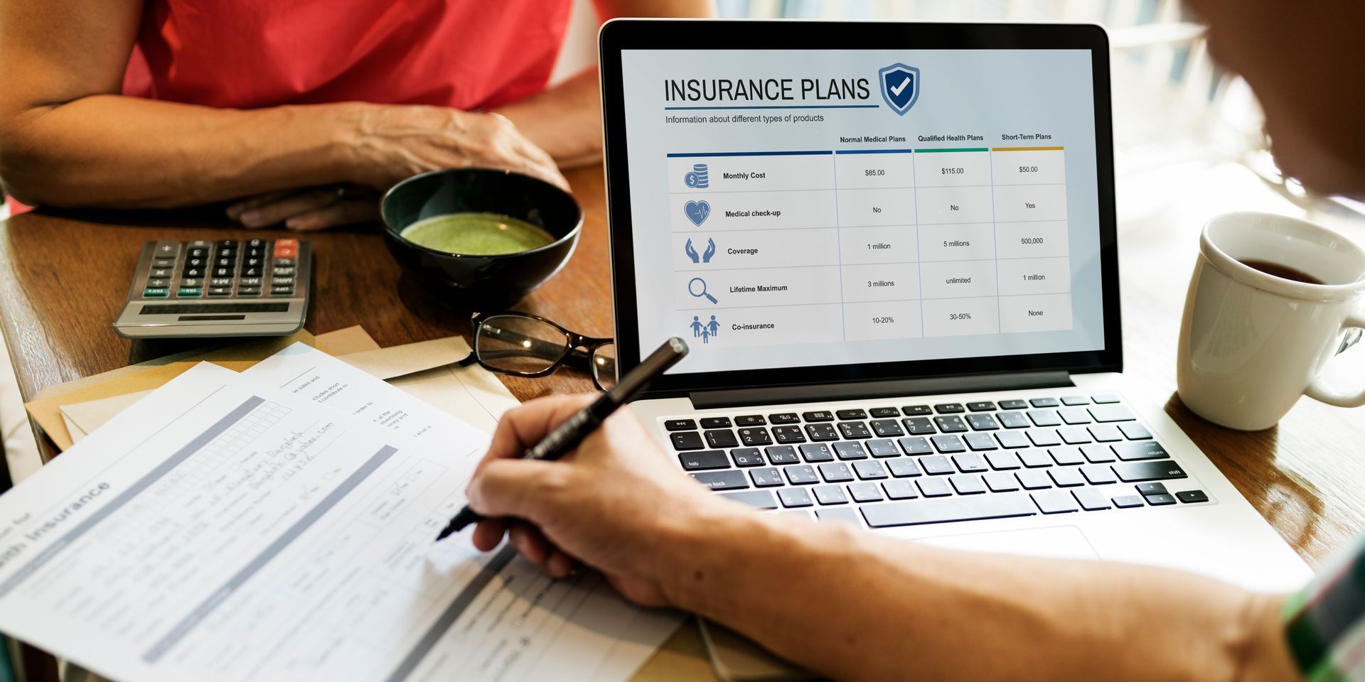 Photograph showing a laptop screen displaying a table of insurance plans with columns for plan features, benefits, and costs.