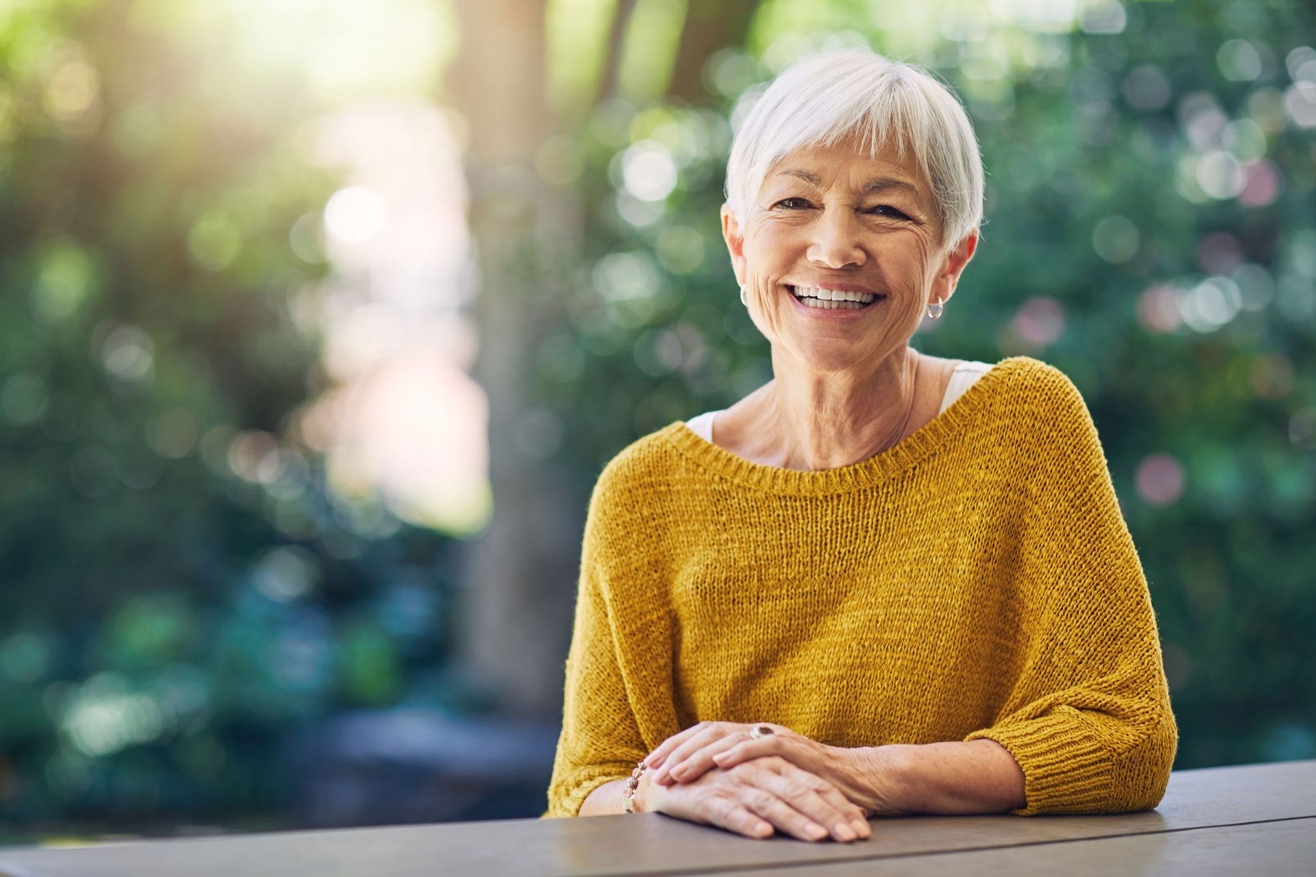 Smiling older Asian woman in yellow sweater outdoors.
